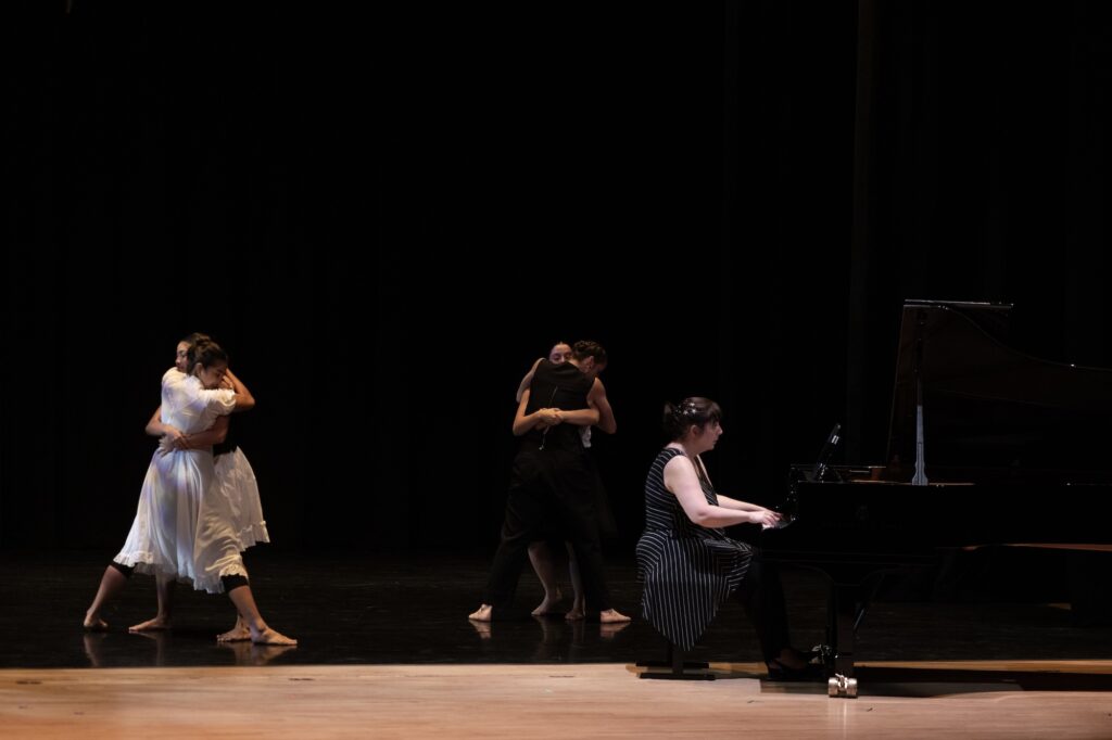 A woman is playing a piano on a stage while dancers perform