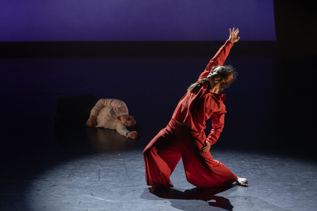 A dancer in all red leaning and reaching to the right