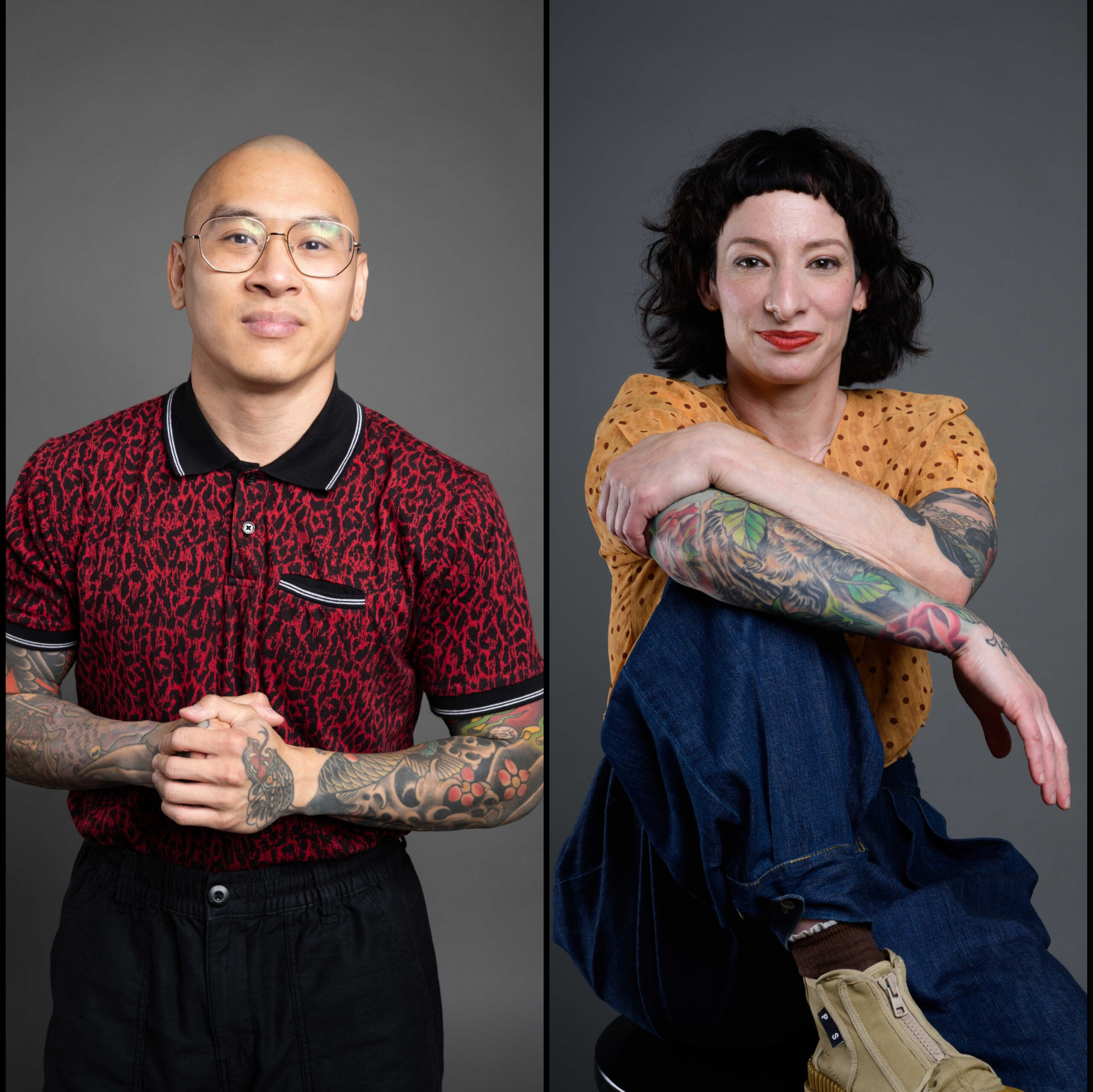 A Vietnamese-American bald man with glasses, in a short sleeved, red and black polo shirt, tattoos filling his forearms, standing with his hands closed together, smiling for a photo and a Jewish-American woman with a bob hairstyle and short bangs, in a short sleeved mustard colored top with floral pattern, tattoos across her arms, blue jeans and tan boots, sits on a chair posing and smiling for a photo.