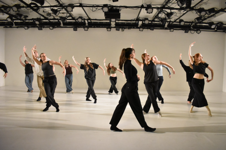 A woman walks past a group of dancers performing in a studio