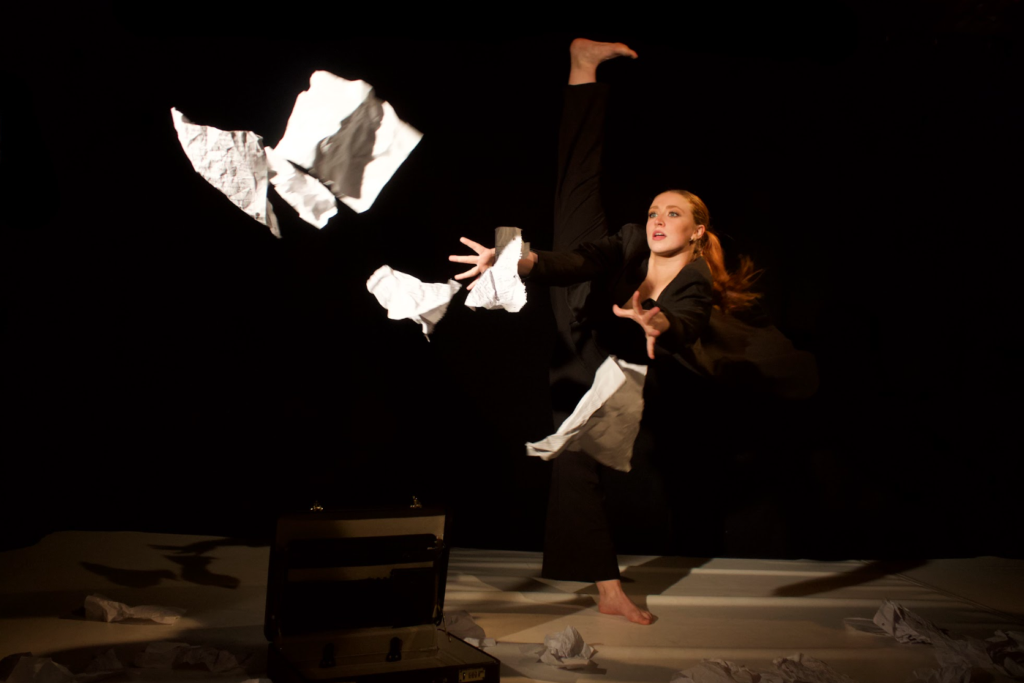 a woman in a dance performance appears to be scrambling trying to grab papers from the air.