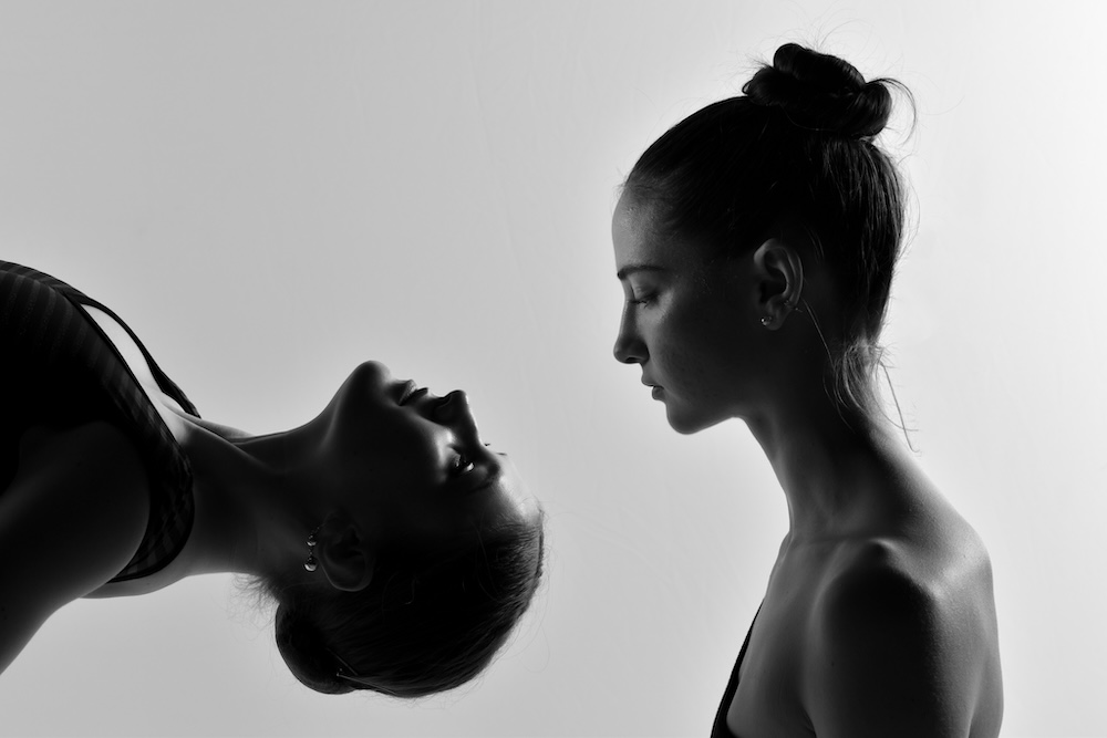 A close up image of one dancer looking down at another dancer who is upside down