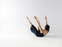 A dancer is on her back, with her arms and legs outstretched, her body curving.