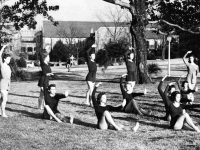 A black and white photo of young women performing in a grassy area on a college campus.