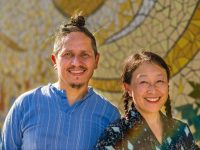 Two people happily pose for a photo in front of a mosaic background